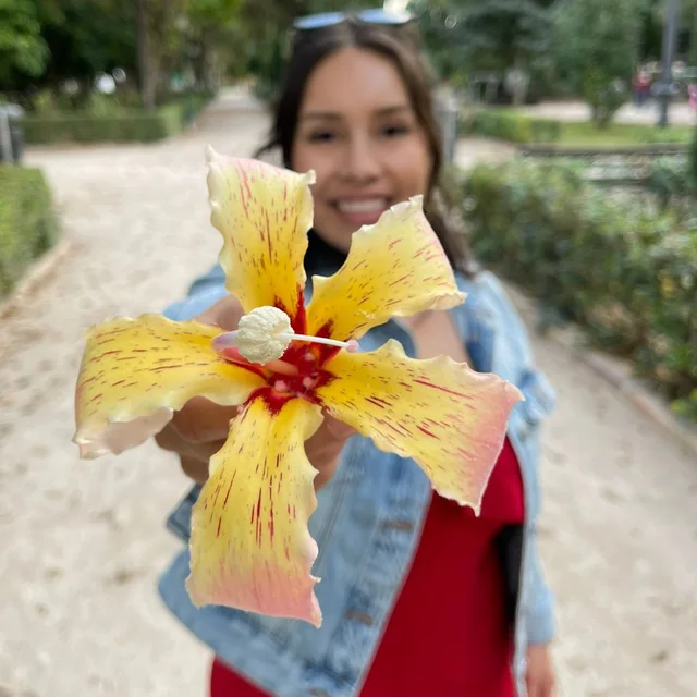 Viv Vivanco smiles and offers a yellow flower toward the camera.